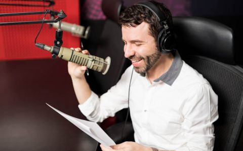 Smiling,Young,Male,Radio,Presenter,With,Headphones,Reading,A,Script